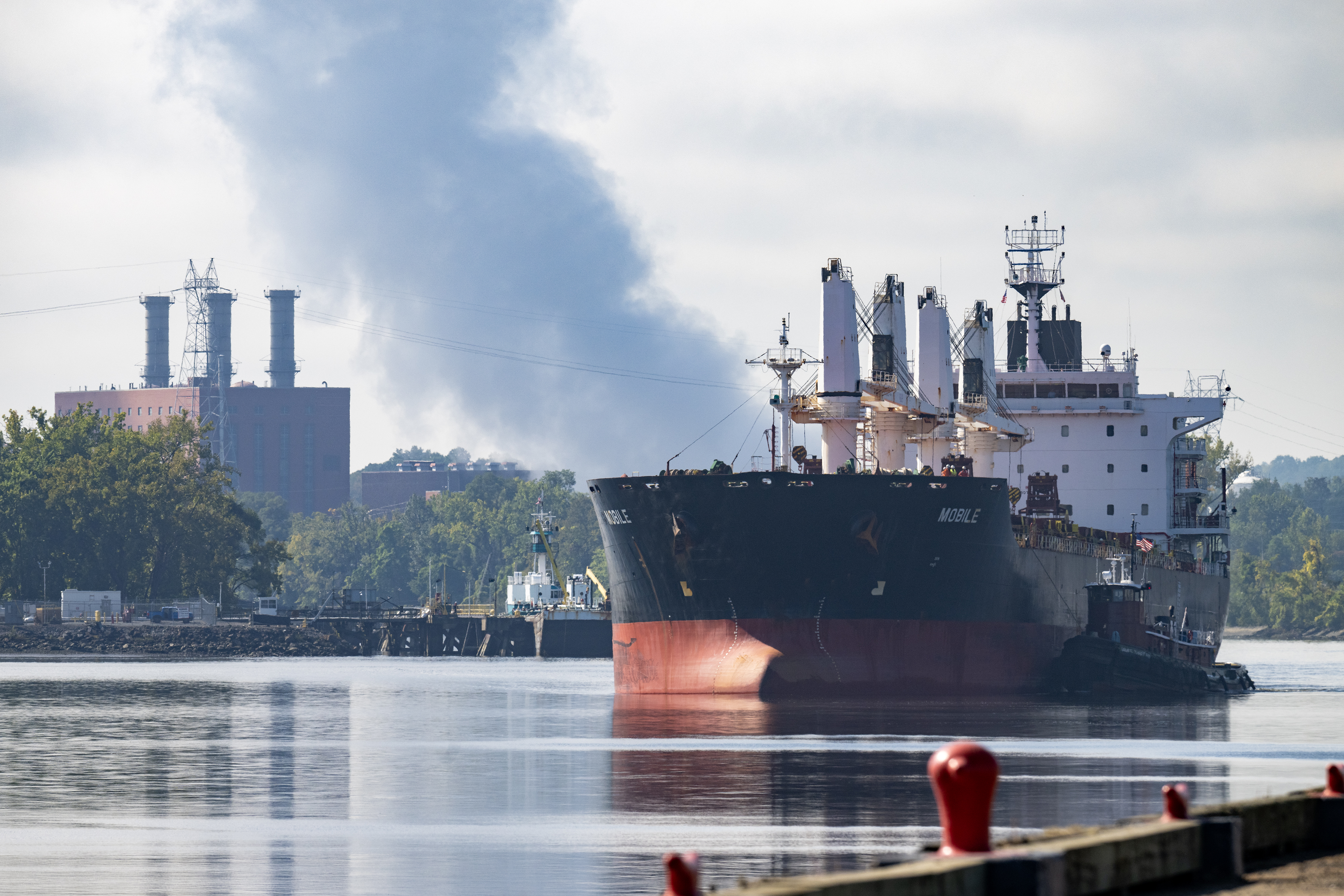 A large boat is sailing away from port, some steam can be seen in the distance.