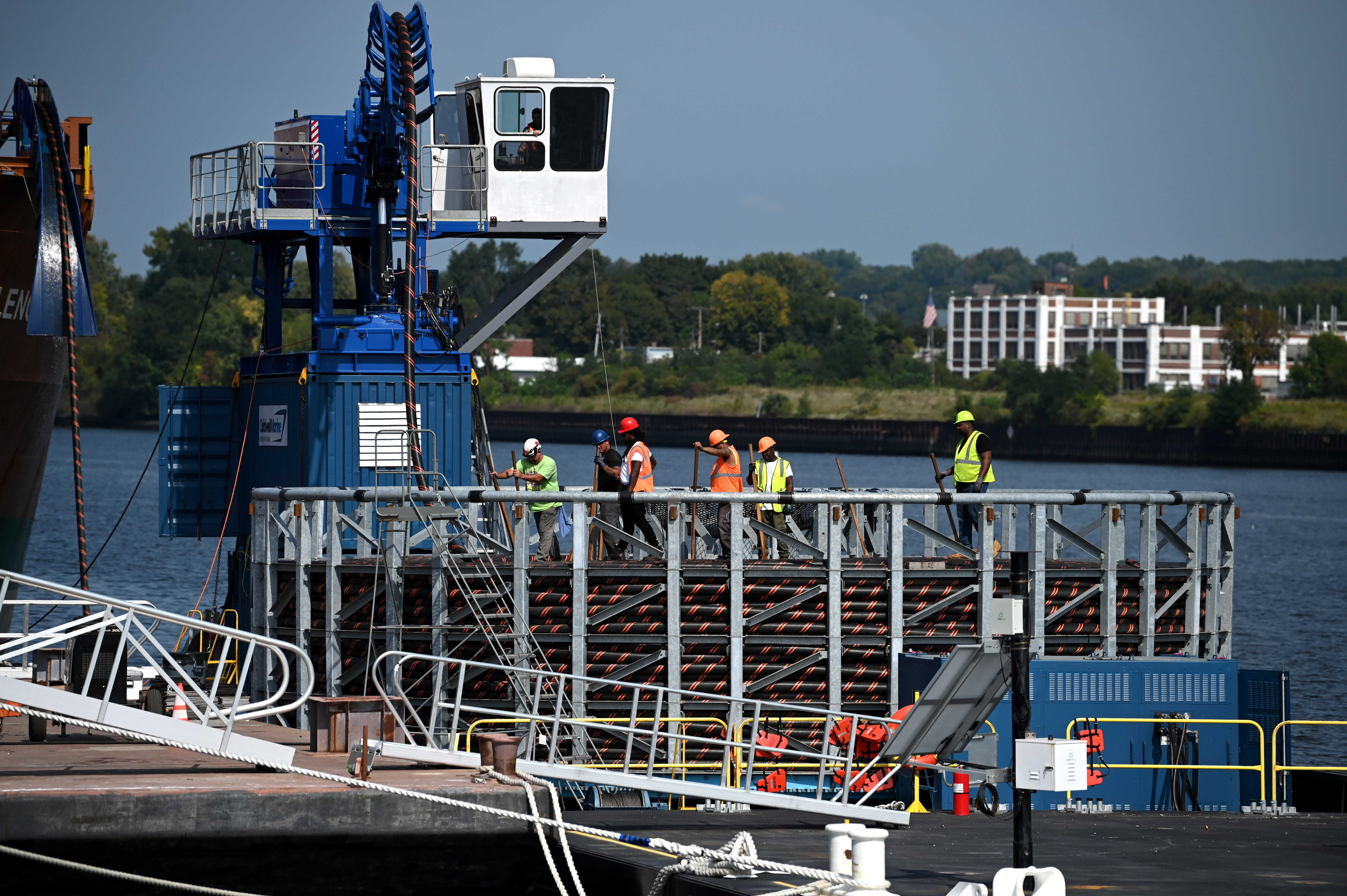 Port workers in high visibility jackets and helmets stand on a dock