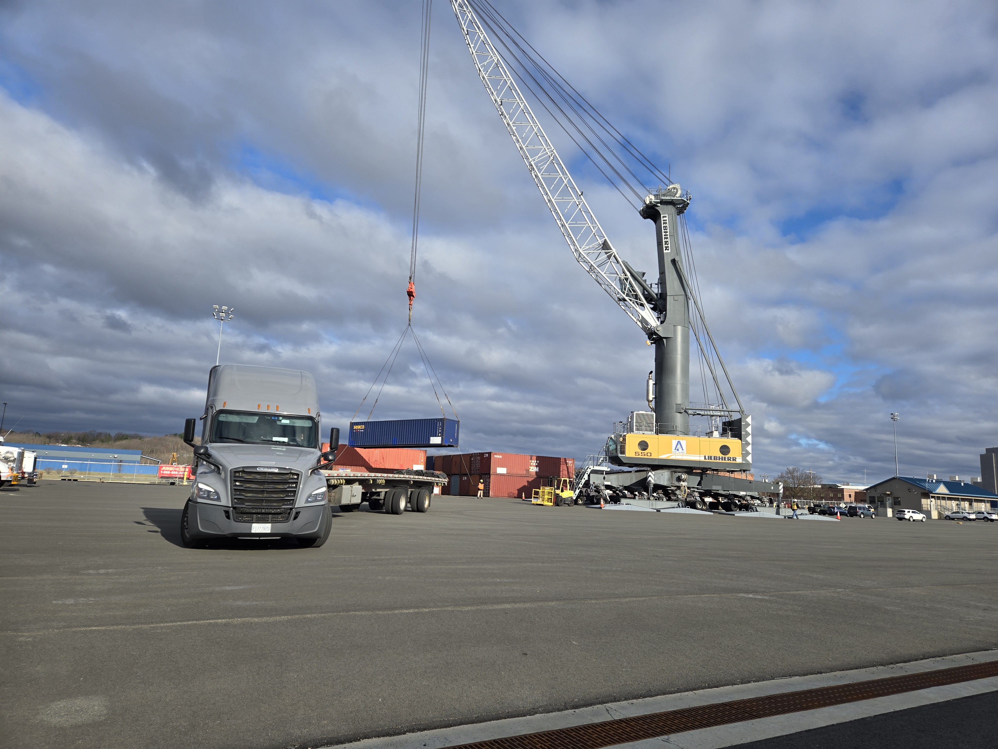Truck in foreground with crane loading container for storage