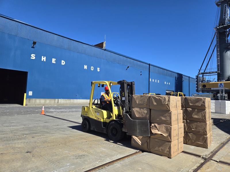 Forklift moving wood pulp in front of Port shed