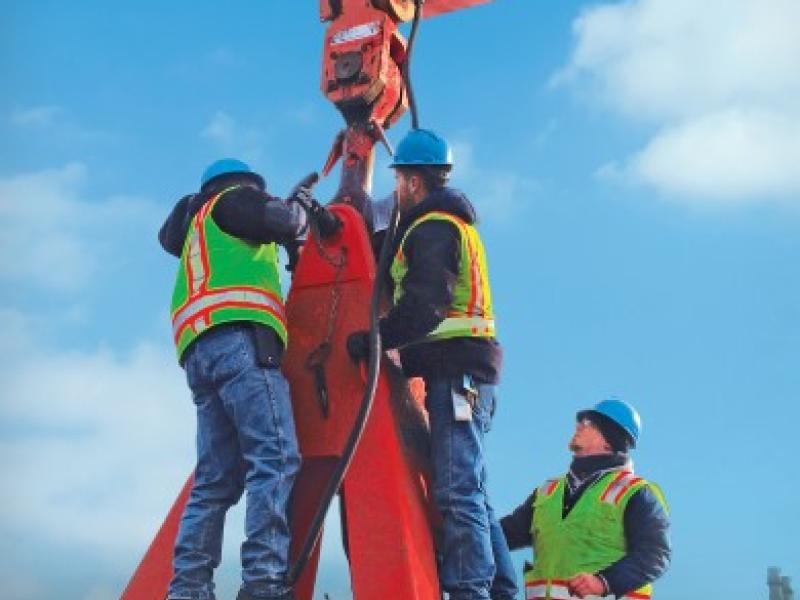 Workers in PPE adjusting hook with bright red support structures