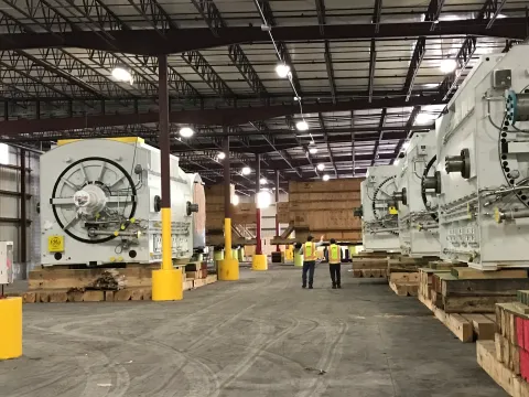 Warehouse storing large generators with two staff in safety yellow