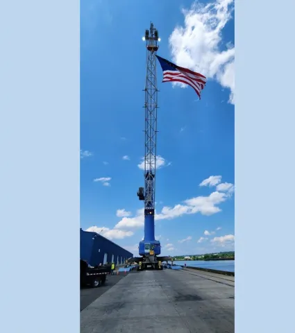 large U.S. flag suspended from crane on the dock with the Hudson River 