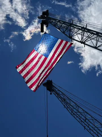 U.S. Flag suspended from crane, backlit by the sun