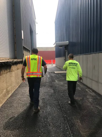 Two workers in safety yellow walking between warehouses 