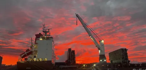 Dramatic red sunrise behind silhouetted ship and crane
