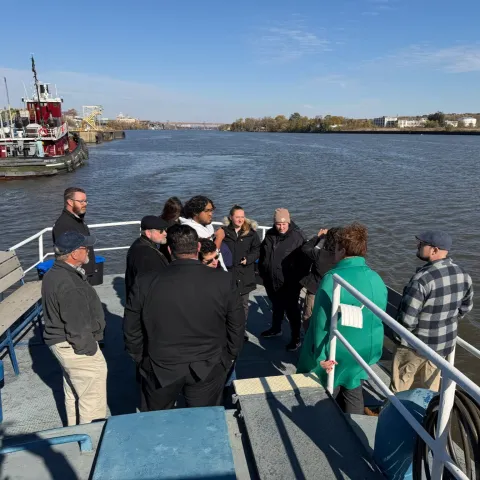 group of UAlbany students on the stern of the Spirit of Albany port boat on the Hudson River with a tugboat in the background 