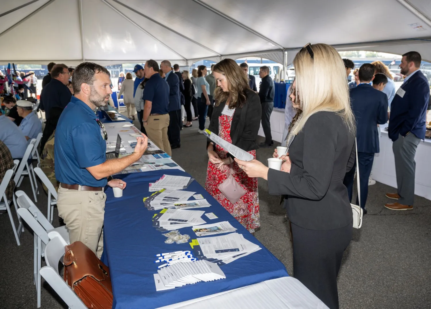 A table at the Port Industry Day with informational handouts and two people listening to someone behind the table talk