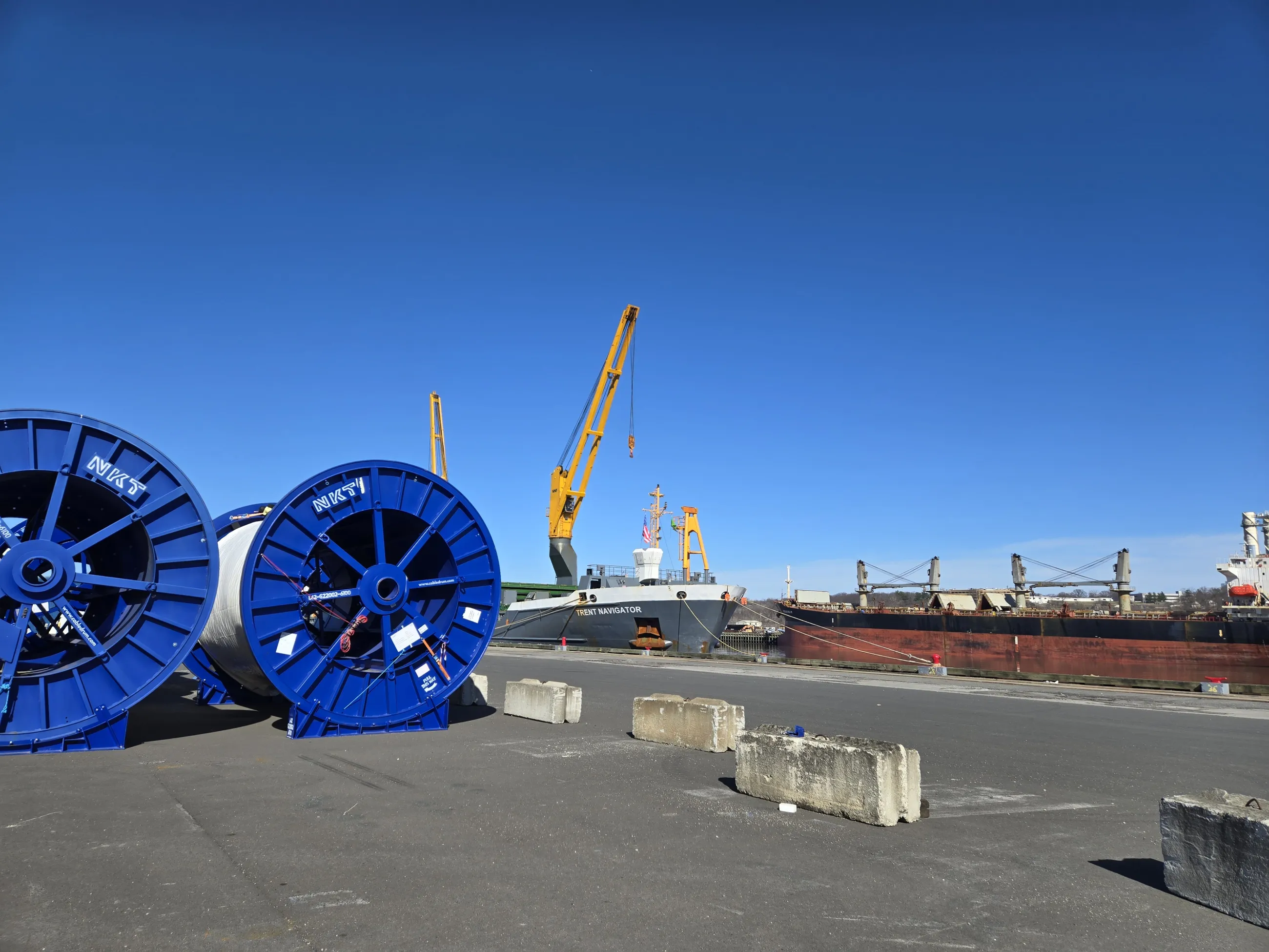 View of the port dock with cranes and a ship in the background and large spools in the foreground