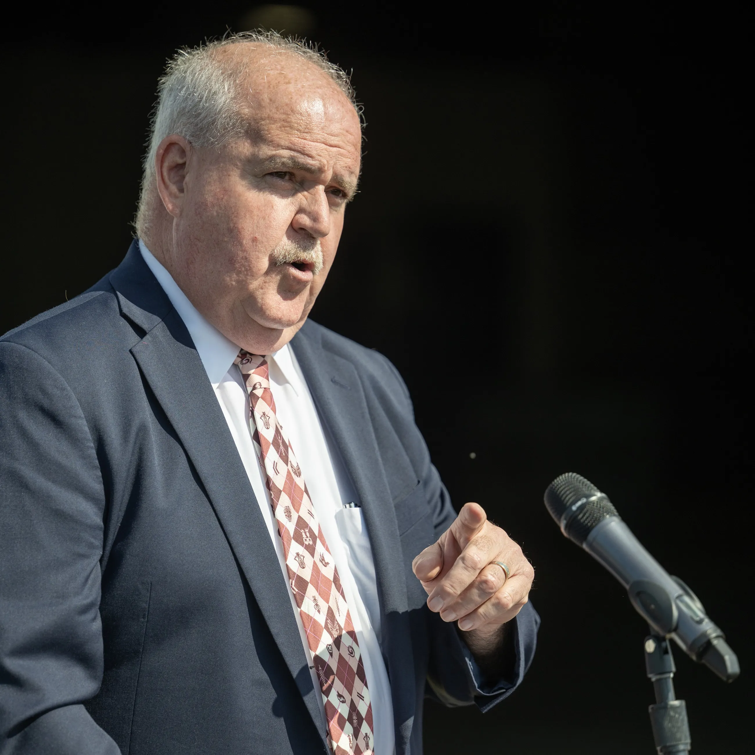 Headshot of CEO Hendrick | man wearing a suit, speaking at a microphone 