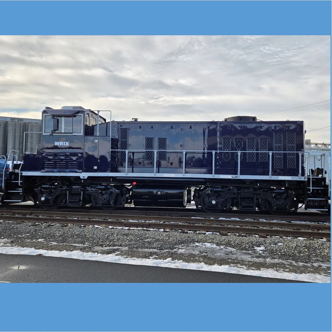 close up of dark blue railroad locomotive with silver accents with a cloudy sky